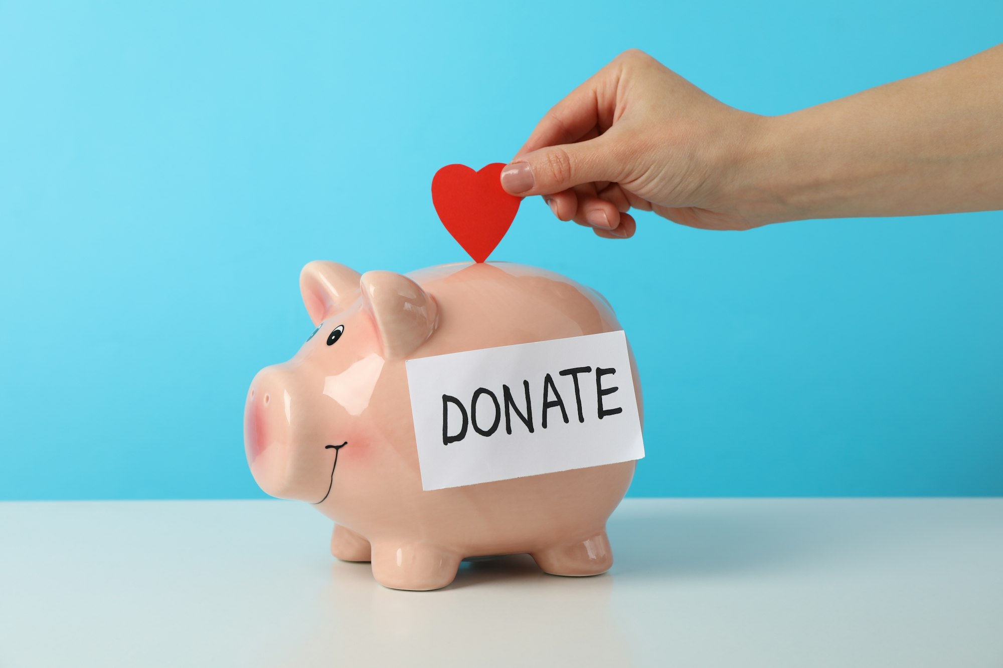 female-hand-puts-heart-in-piggy-bank-with-text-donate-against-blue-background.jpg